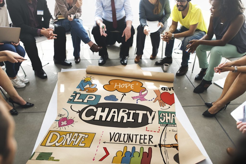 Wolontariusze fundacji siedzą w kręgu wokół plakatu z hasłami charity, donate i volunteer